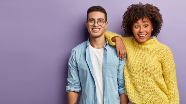 Jovem casal sorrindo positivamente, contando boas notícias, sobre o fundo roxo. Mulher feliz se inclinando no ombro do colega.