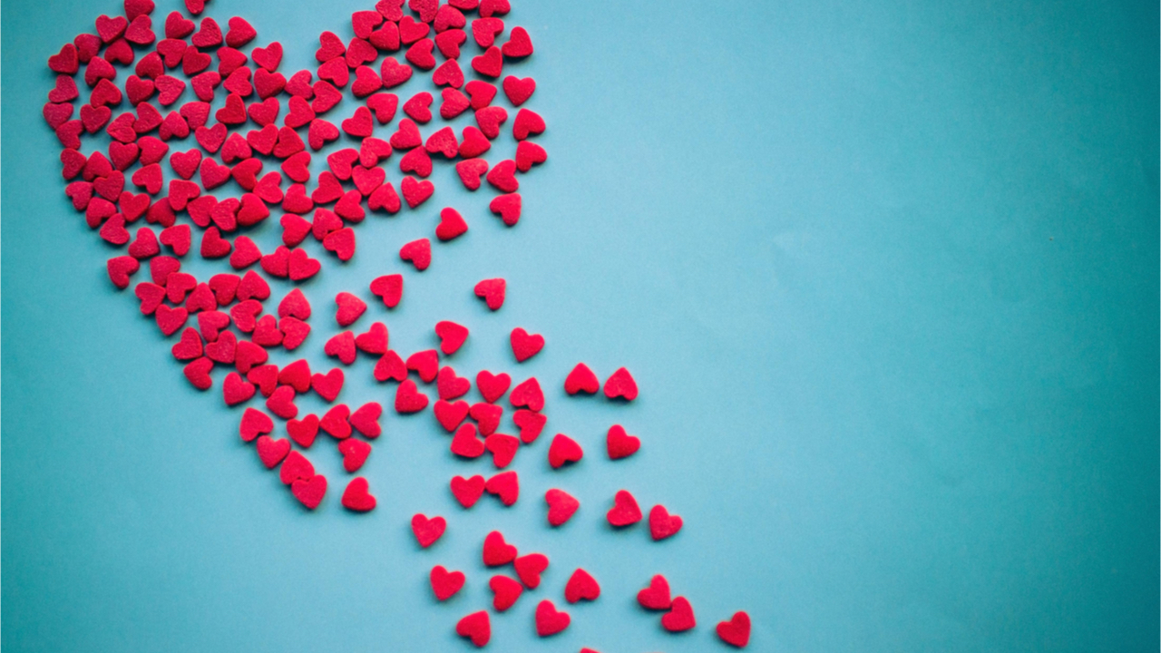 Em um fundo azul, um grande coração vermelho se divide em pedaços. Amor infeliz, sentimentos não correspondidos, decepção.