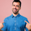 Homem com camisa azul orgulhoso e auto-satisfeito em fundo rosa.