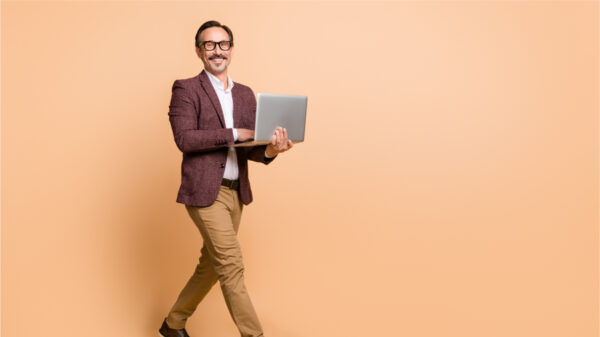 Corpo inteiro de um homem usando laptop, isolado sobre o fundo de cor bege.