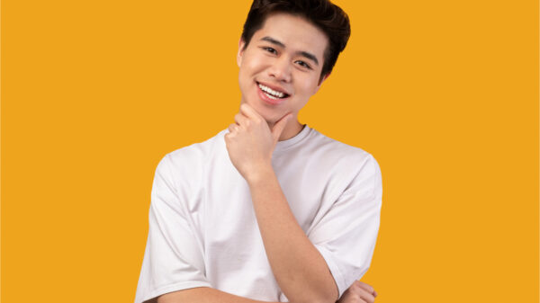 Retrato masculino casual. Homem alegre e sorridente olhando para a câmera, tocando o queixo, vestindo camisa branca, isolado sobre fundo laranja do estúdio. Feliz modelo adolescente casual masculino posando.