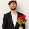 homem vestindo terno e segurando um buquê de rosas vermelhas em fundo claro