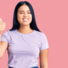 Jovem garota vestindo roupas casuais, sorrindo feliz e positiva, com o polegar para cima, fazendo sinal de aprovação.