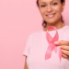 Mulher sorridente de camiseta rosa segurando uma fita de cetim na mão. Conscientização do câncer de mama, outubro rosa, fundo colorido. Conceito de apoio ao câncer de mama.