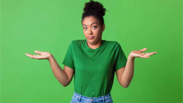 Retrato de uma jovem encolhendo os ombros, olhando para a câmera posando sobre fundo verde. Foto de estúdio. Mulher intrigada.