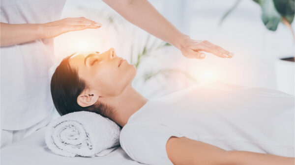 Foto de curandeiro reiki fazendo sessão de terapia para acalmar jovem com os olhos fechados.