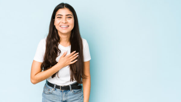 mulher de blusa branca com a mão no peito em fundo azul claro
