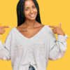 Mulher vestindo roupas casuais, parecendo confiante, com um sorriso no rosto, apontando-se com os dedos, orgulhosa e feliz.