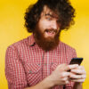 Jovem barbudo surpreso usando celular. Homem de barba surpreso. Homem com cabelo encaracolado e barba.