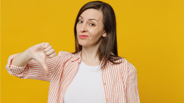 mulher fazendo sinal de negativo com o polegar em fundo amarelo