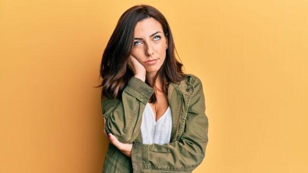 mulher com a cabeça apoiada nas mãos e fazendo careta em fundo laranja
