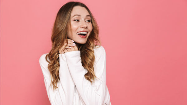 mulher de blusa branca com as mãos juntas e em fundo rosa