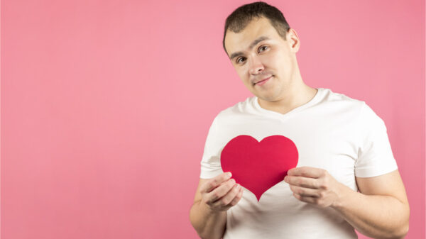 Um homem em um fundo rosa com um coração de papel vermelho. Um homem dando seu amor, confessando seu amor.
