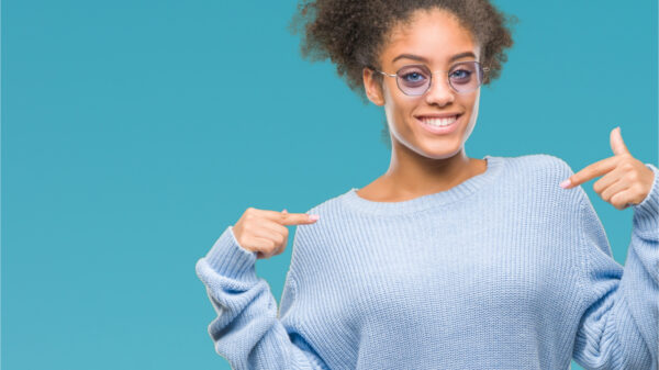 Jovem de óculos sobre fundo isolado, parecendo confiante, com um sorriso no rosto, apontando-se com os dedos, orgulhosa e feliz.