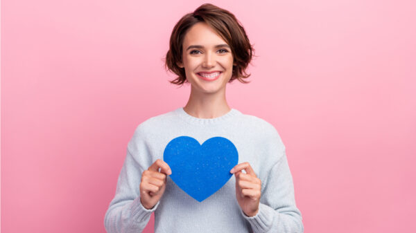 mulher vestindo blusa branca e segurando um coração azul de papel em fundo rosa
