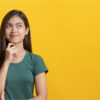 Adolescente em camiseta verde pensando/imaginando/perguntando-se isolada em fundo amarelo no estúdio.