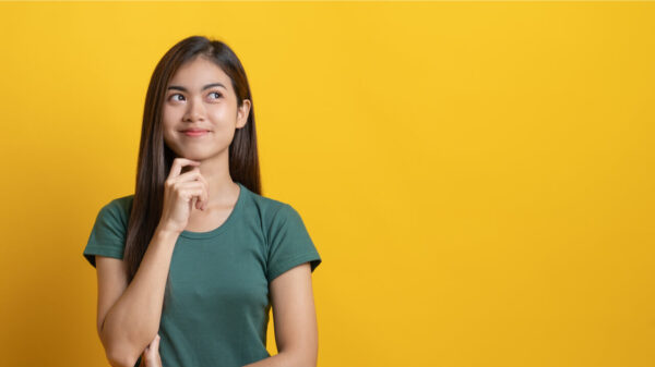 Adolescente em camiseta verde pensando/imaginando/perguntando-se isolada em fundo amarelo no estúdio.