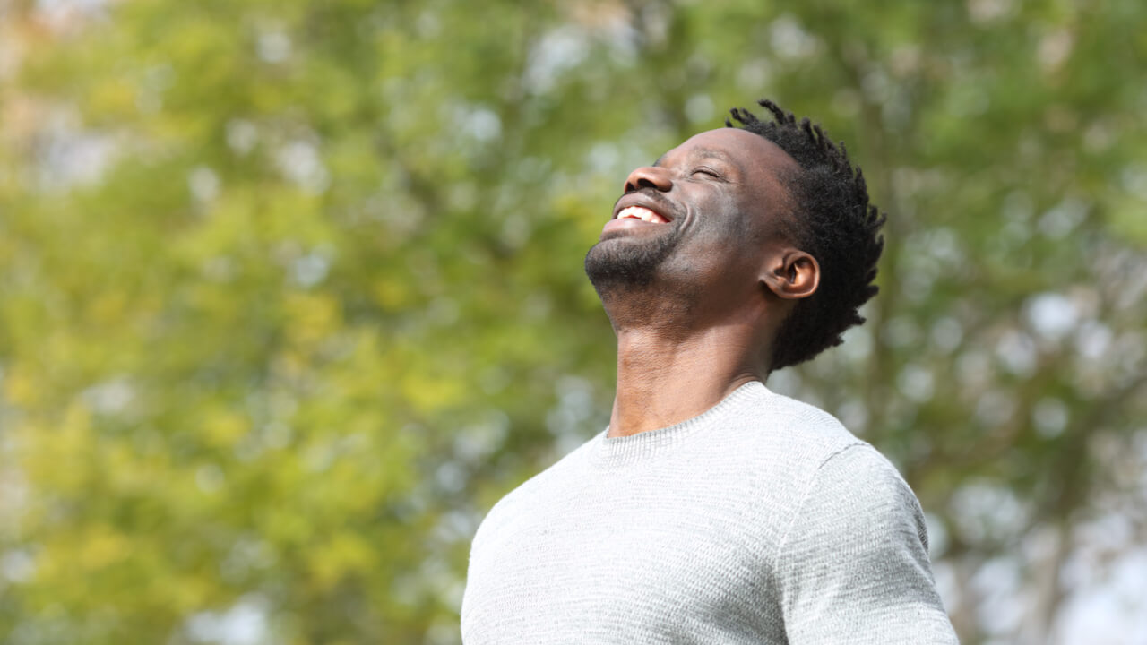 homem negro sorrindo com árvores desfocadas ao fundo