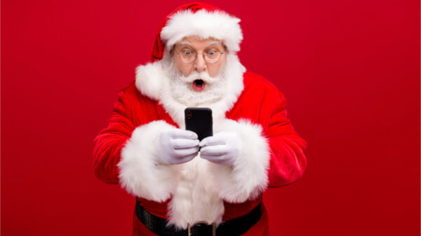 Retrato de homem vestido de Papai Noel usando celular, isolado sobre fundo de cor vermelha.