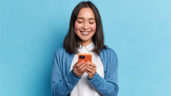 Mulher morena sorridente usando celular, isolada sobre fundo azul. Comunicação online.