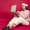 Mulher surpresa parecendo animada enquanto usa gorro de natal e mexe no computador.