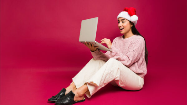 Mulher surpresa parecendo animada enquanto usa gorro de natal e mexe no computador.