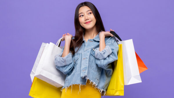 mulher segurando várias sacolas de compra em fundo roxo