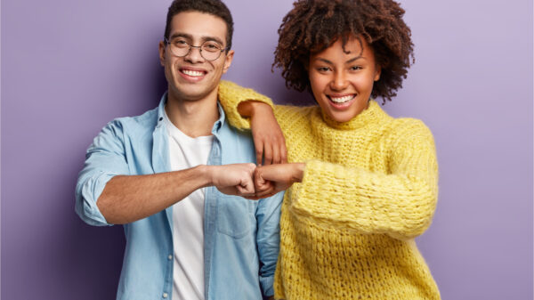 Parceiros dão um soquinho na mão do outro, concordam em trabalhar juntos, têm expressões faciais felizes, isolados sobre fundo roxo. Conceito de trabalho em equipe.