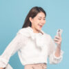Mulher jovem com roupa casual usando smartphone em fundo azul.