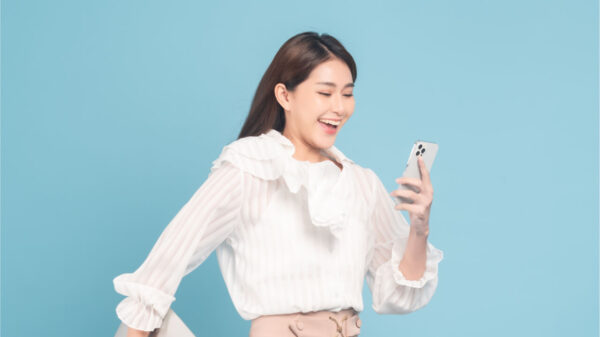 Mulher jovem com roupa casual usando smartphone em fundo azul.