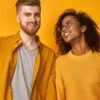 Expressões faciais e conceito de emoções positivas. Mulher feliz e sorridente e homem em roupas casuais, sorriem alegremente, satisfeitos em passar o tempo livre juntos, isolados na parede laranja.