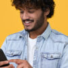 Jovem feliz usando telefone celular isolado em fundo amarelo. Homem sorridente segurando smartphone.