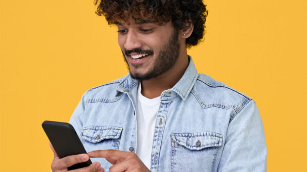Jovem feliz usando telefone celular isolado em fundo amarelo. Homem sorridente segurando smartphone.