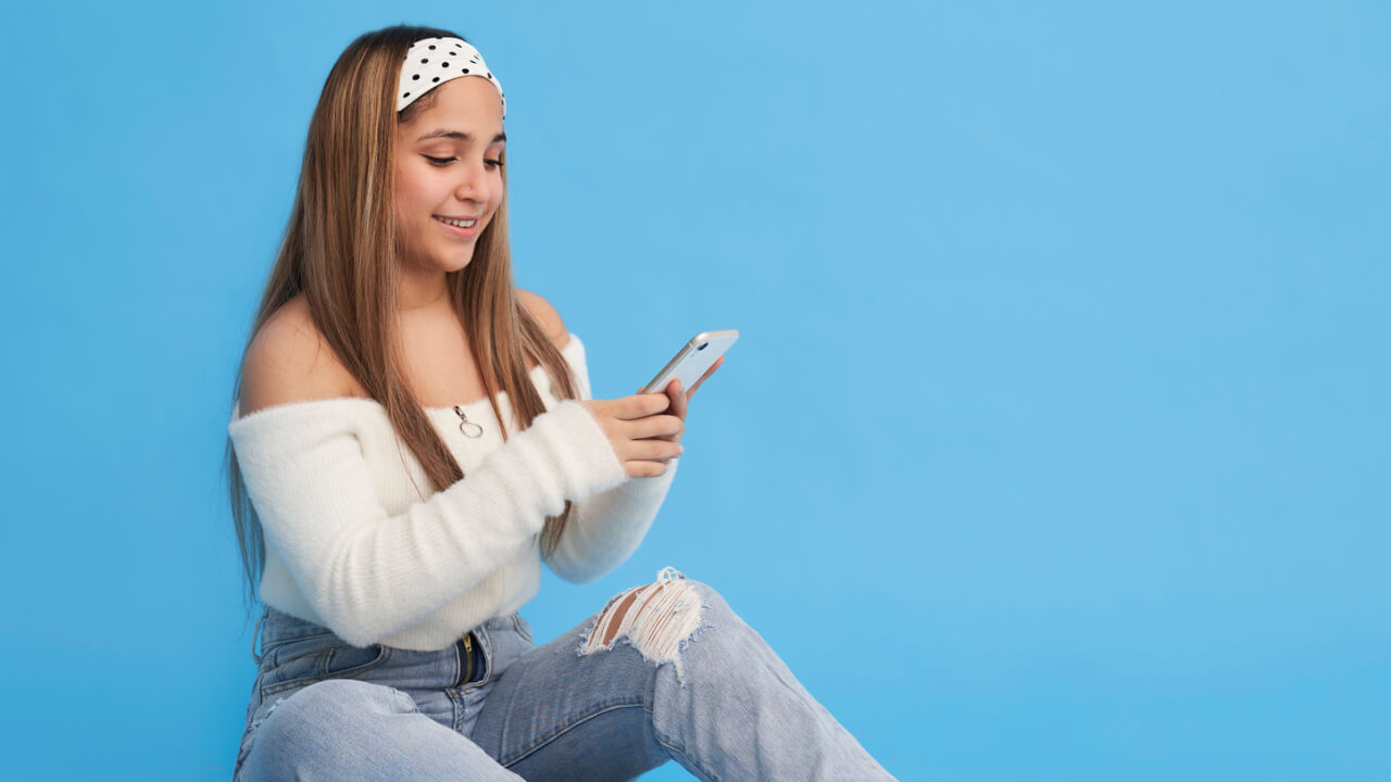 Jovem sentada no chão usando celular.
