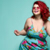 Mulher de óculos de sol da moda e vestido de verão colorido dançando feliz, comemorando em fundo verde.