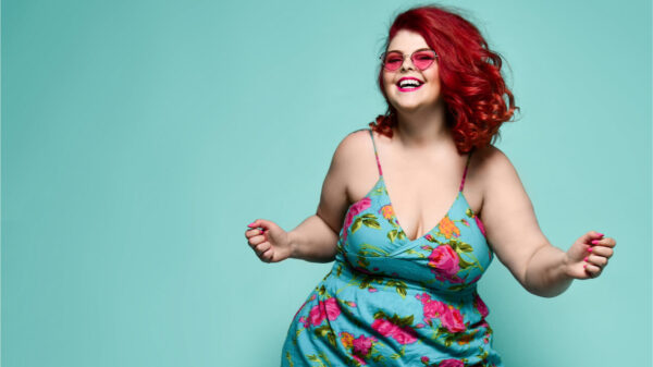Mulher de óculos de sol da moda e vestido de verão colorido dançando feliz, comemorando em fundo verde.