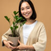 Mulher segurando planta em fundo bege. Garota feliz posando com planta em pano de fundo isolado.