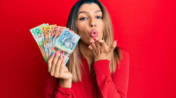 Mulher morena segurando dólares australianos, olhando para a câmera, mandando um beijo com a mão no ar, sendo adorável. Expressão de amor.