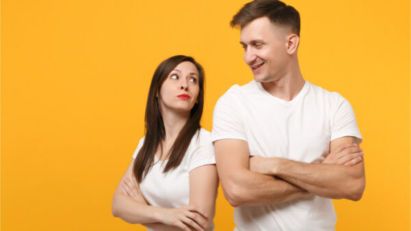 Jovem casal de blusas brancas posando isolados no fundo da parede amarela/laranja. Conceito de estilo de vida de pessoas. Braços cruzados.