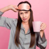 Foto de mulher infeliz e mal-humorada segurando caneca de café, isolada sobre o fundo de cor rosa.