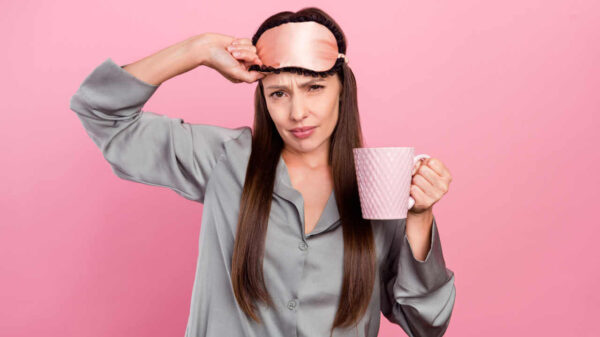 Foto de mulher infeliz e mal-humorada segurando caneca de café, isolada sobre o fundo de cor rosa.