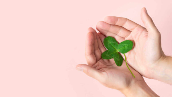 Uma mão segurando um trevo de quatro folhas em um fundo rosa. Símbolo de fortuna, felicidade e sucesso.