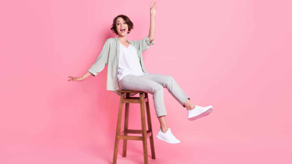 Foto de comprimento total de mulher sentada e isolada no fundo rosa.