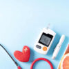 Vista superior de alimentos saudáveis no prato com estetoscópio e coração vermelho para dieta de colesterol e controle de diabetes em fundo azul pastel.