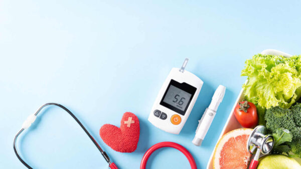 Vista superior de alimentos saudáveis no prato com estetoscópio e coração vermelho para dieta de colesterol e controle de diabetes em fundo azul pastel.