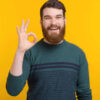 Retrato de um jovem fazendo gesto de "ok" sobre fundo amarelo.