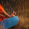 Pessoa em posição de lótus na natureza, nas montanhas, sentada na grama ao pôr do sol, meditando com mantras, gesto de mão zen.