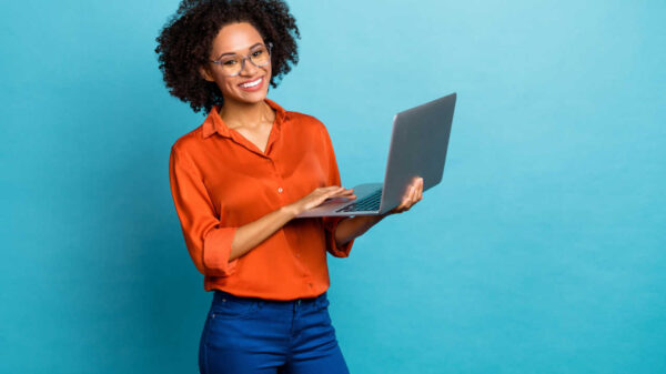 Retrato de uma mulher alegre de cabelos cacheados usando laptop, isolada em fundo de cor azul.
