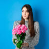 Garota no espaço vazio, segurando um buquê de rosas cor de rosa, sozinha no fundo azul.