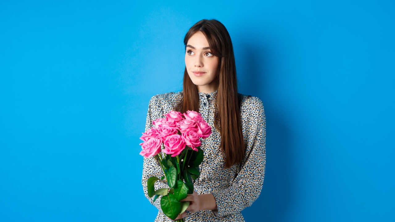 Garota no espaço vazio, segurando um buquê de rosas cor de rosa, sozinha no fundo azul.